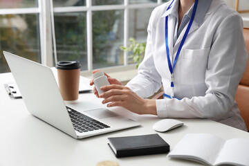 Female doctor with pill bottle working at table in clinic, closeup