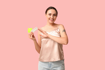 Beautiful young woman with condom and birth control pills on pink background. Safe sex concept