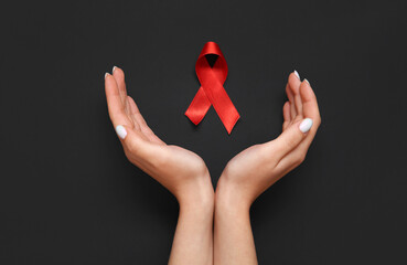 Female hands with red ribbon on black background. AIDS Day concept