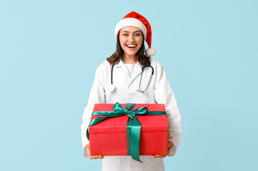 Beautiful female doctor in Santa hat with gift box on blue background