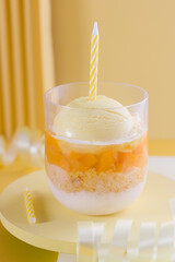 Glass with ice cream, chopped fruit, cake and Greek yogurt with happy birthday decoration.