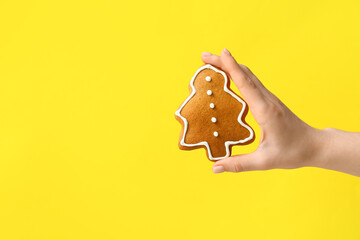 Female hand with sweet Christmas cookie on yellow background
