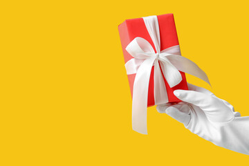 Female hand with Christmas gift box on yellow background