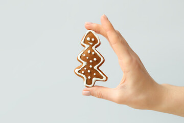 Female hand with sweet Christmas cookie on grey background
