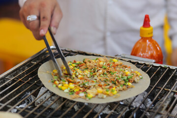 Man cooking grilled vietnamese pancake with eggs sausages and sauces in food festival