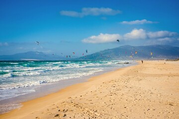 Soaring kite surfers and beach with Atlantic ocean and golden sand on background of mountains.
