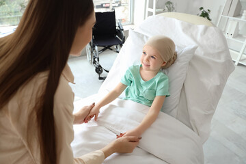 Little girl after chemotherapy with her mother holding hands in clinic - obrazy, fototapety, plakaty