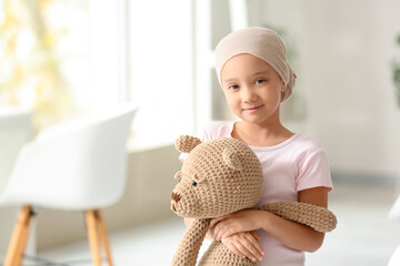 Little Asian girl after chemotherapy with toy bear in clinic