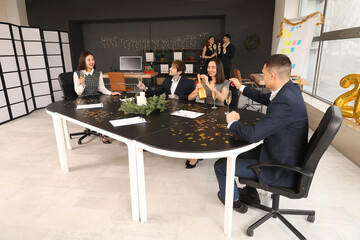 Group of young business people with champagne celebrating New Year at table in office