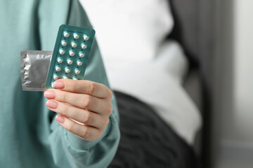 Woman holding condom and contraceptive pills on blurred background, closeup with space for text....