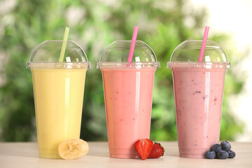 Plastic cups with different tasty smoothies and fresh fruits on wooden table outdoors