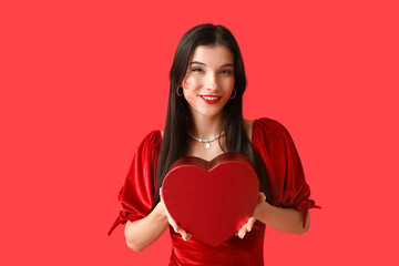 Happy young woman with kiss marks on her face and gift box on red background