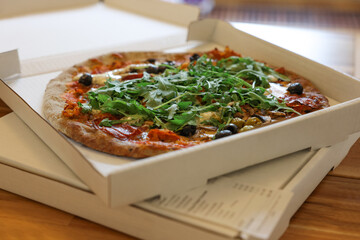 Delicious pizza with arugula, mushrooms and olives in box on wooden table, closeup