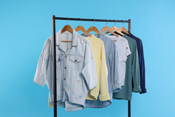 Rack with stylish clothes on wooden hangers against light blue background