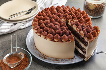 Delicious tiramisu cake with cocoa powder and server on grey table