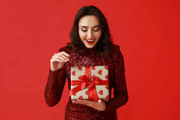 Surprised young woman with gift box on red background