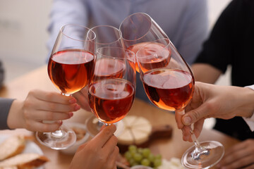 People clinking glasses with rose wine above table indoors, closeup