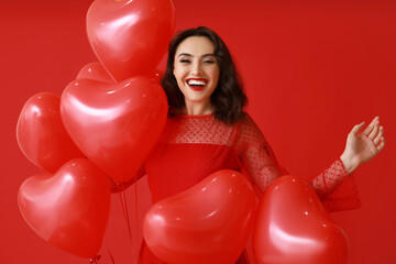 Happy young woman with heart shaped air balloons on red background