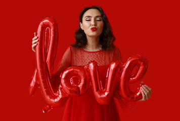 Beautiful young woman with air balloons in shape of word LOVE on red background