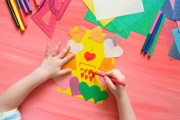 Little girl making card for grandma. Colorful pink background with paper decoration, multicolored...