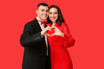 Loving young couple showing heart gesture on red background. Celebration of Saint Valentine's Day