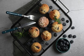 Delicious muffins with powdered sugar, blueberries and cutlery on light grey table, flat lay