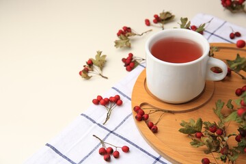 Cup with hawthorn tea and berries on beige table, space for text