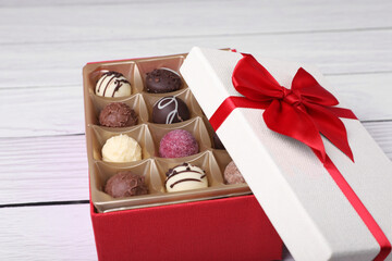 Red box with tasty chocolate candies on white wooden table, closeup