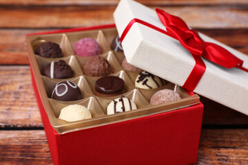 Red box with tasty chocolate candies on wooden table, closeup