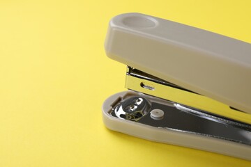 Beige stapler on yellow background, closeup. Space for text