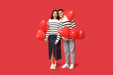Loving young couple with heart-shaped balloons on red background. Celebration of Saint Valentine's...