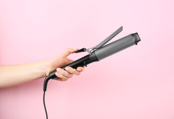 Hair styling appliance. Woman holding curling iron on pink background, closeup