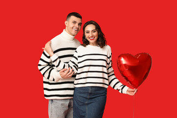 Loving young couple with heart-shaped balloon on red background. Celebration of Saint Valentine's...