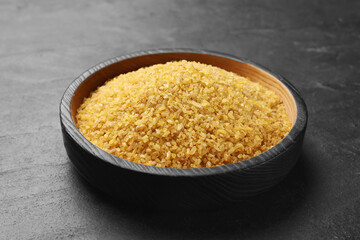 Raw bulgur in bowl on dark gray table, closeup