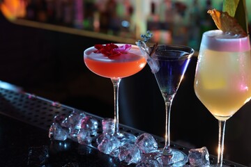 Different fresh alcoholic cocktails and ice cubes on counter in bar. Space for text