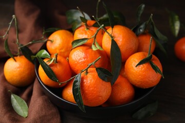 Fresh ripe tangerines with green leaves in bowl on table, closeup