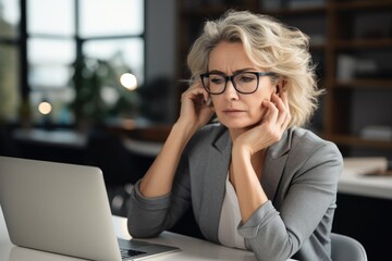 Worried, fatigued, tired, exhausted, mature,businesswoman, wearing, glasses, in front of a lap top working - obrazy, fototapety, plakaty