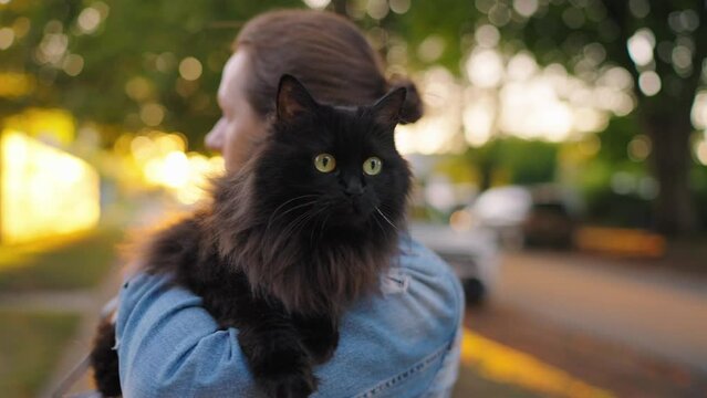 Beautiful woman holding and hugging her black cat outdoor.