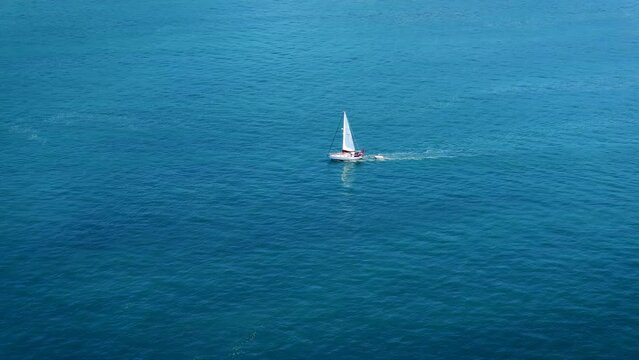 Aerial footage of sailboat sailing on a deep blue sea with white waves