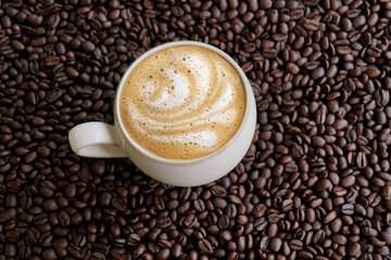 Cafe latte with foam design on a coffee beans background and dramatic light