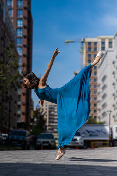 Beautiful Asian ballerina in blue dress posing in splits outdoors. Urban landscape. Vertical photo. 