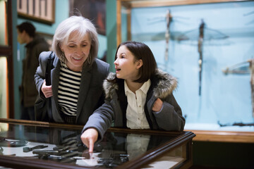 Interested preteen girl visiting history museum of with grandmother, viewing ancient handguns in...