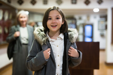 Portrait of interested cheerful preteen girl looking at exposition in historical museum..