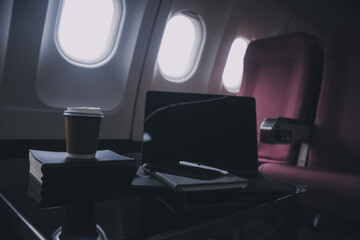 Naklejka premium Attractive asian female passenger of airplane sitting in comfortable seat listening music in earphones while working at modern laptop computer with mock up area using wireless connection on board.