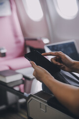 Asian woman passenger sitting in airplane near window and reading news from social networks or using travel applications in smartphone