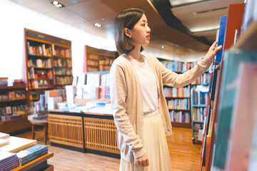Portrait of young adult southeast asian woman reading book at bookstore shop - obrazy, fototapety, plakaty