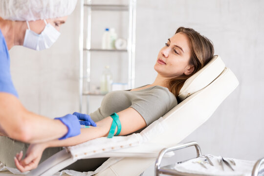 Professional elderly doctor in scrub drawing blood from young patient.