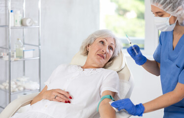 Female nurse injecting needle in hand of elderly patient at hospital. She is lying calm.