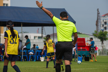 Professional soccer referee on a  youth soccer tournament. Seeing kids in the pitch playing a match with lots of intense and passion. - obrazy, fototapety, plakaty