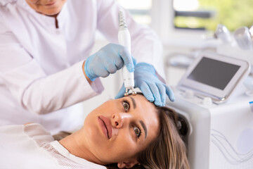 Young adult woman receiving facial radiofrequency procedure stimulating collagen production...